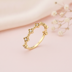gold ring with four-petaled floral motifs and clear center stones along the band on blush silk with dried flowers