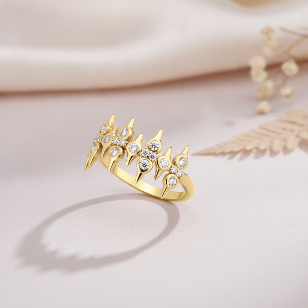 sculpted gold statement ring with pointed crests and clear round stones on blush pink fabric with a dried fern leaf