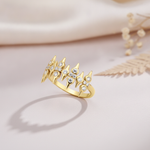 sculpted gold statement ring with pointed crests and clear round stones on blush pink fabric with a dried fern leaf