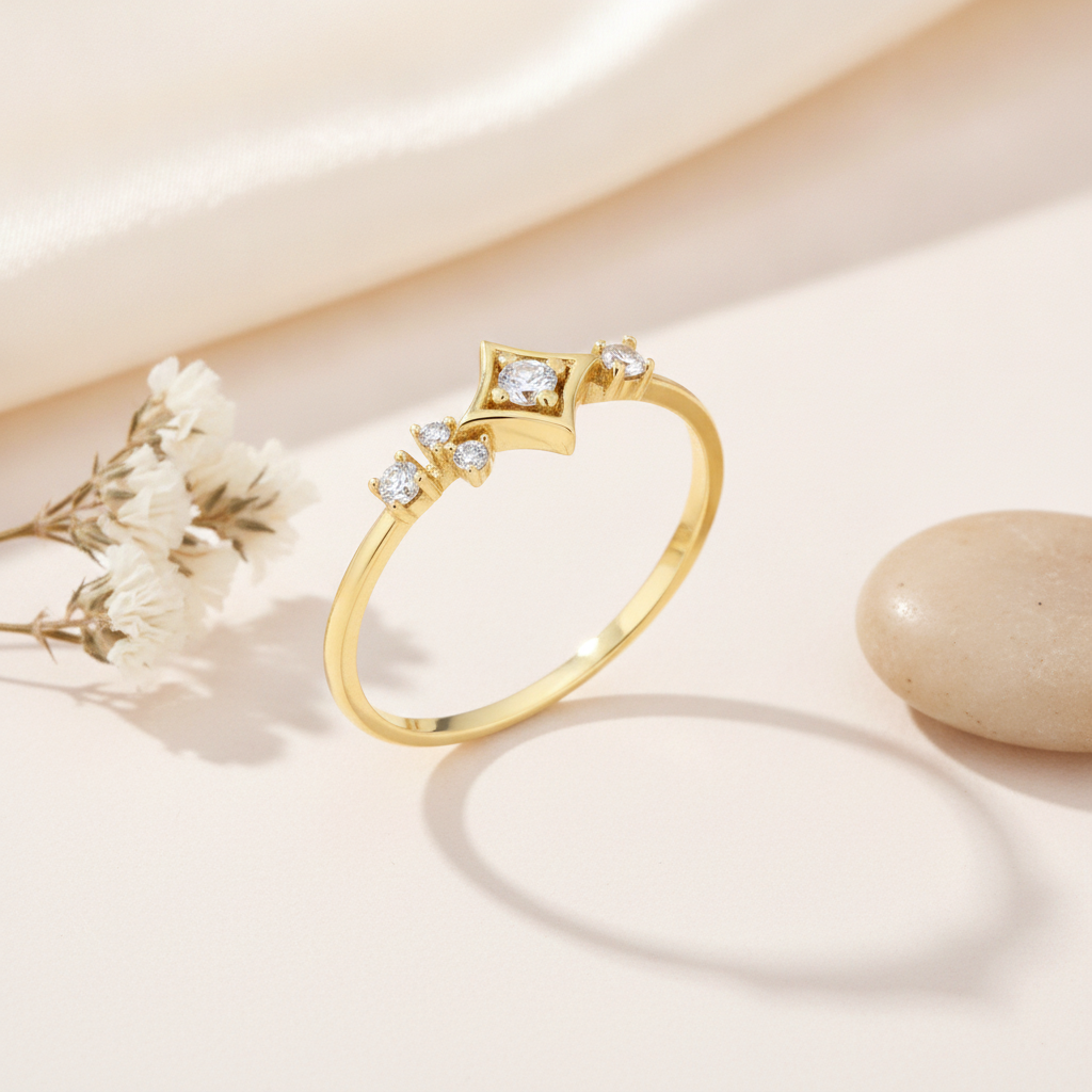 gold ring with a four-pointed star setting and an asymmetrical trail of clear accent stones on blush silk with dried flowers and a pebble