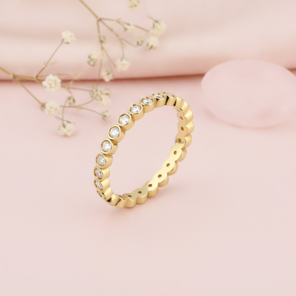 gold eternity ring with continuous round bezel-set clear stones on blush silk with dried flowers and a rose quartz stone