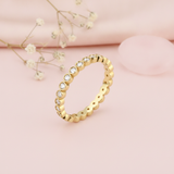 gold eternity ring with continuous round bezel-set clear stones on blush silk with dried flowers and a rose quartz stone