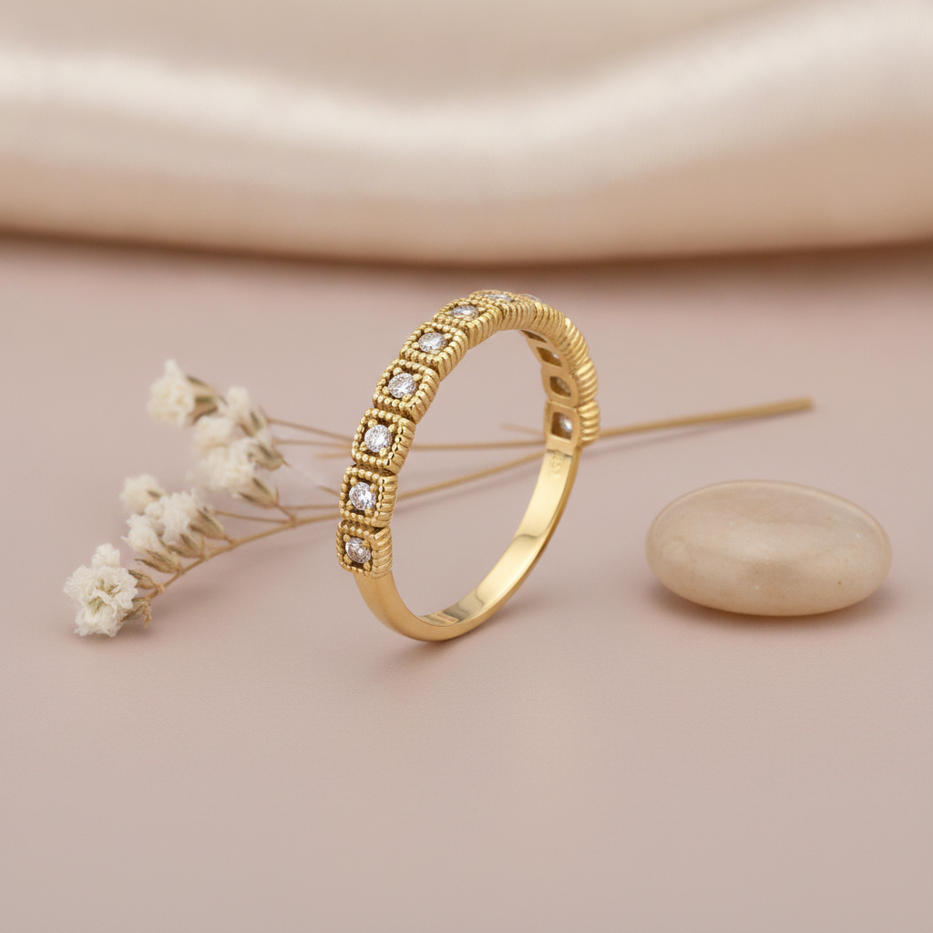 gold ring with alternating raised segments and square-set clear stones on blush silk with dried flowers and a pebble