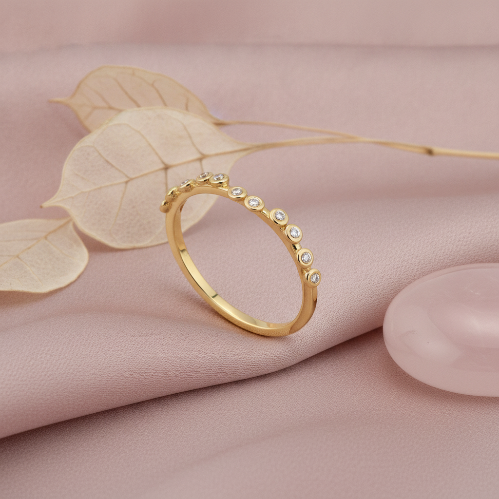 gold ring dotted with small bezel-set clear stones along a wavy band on blush silk with dried flowers and a rose quartz stone