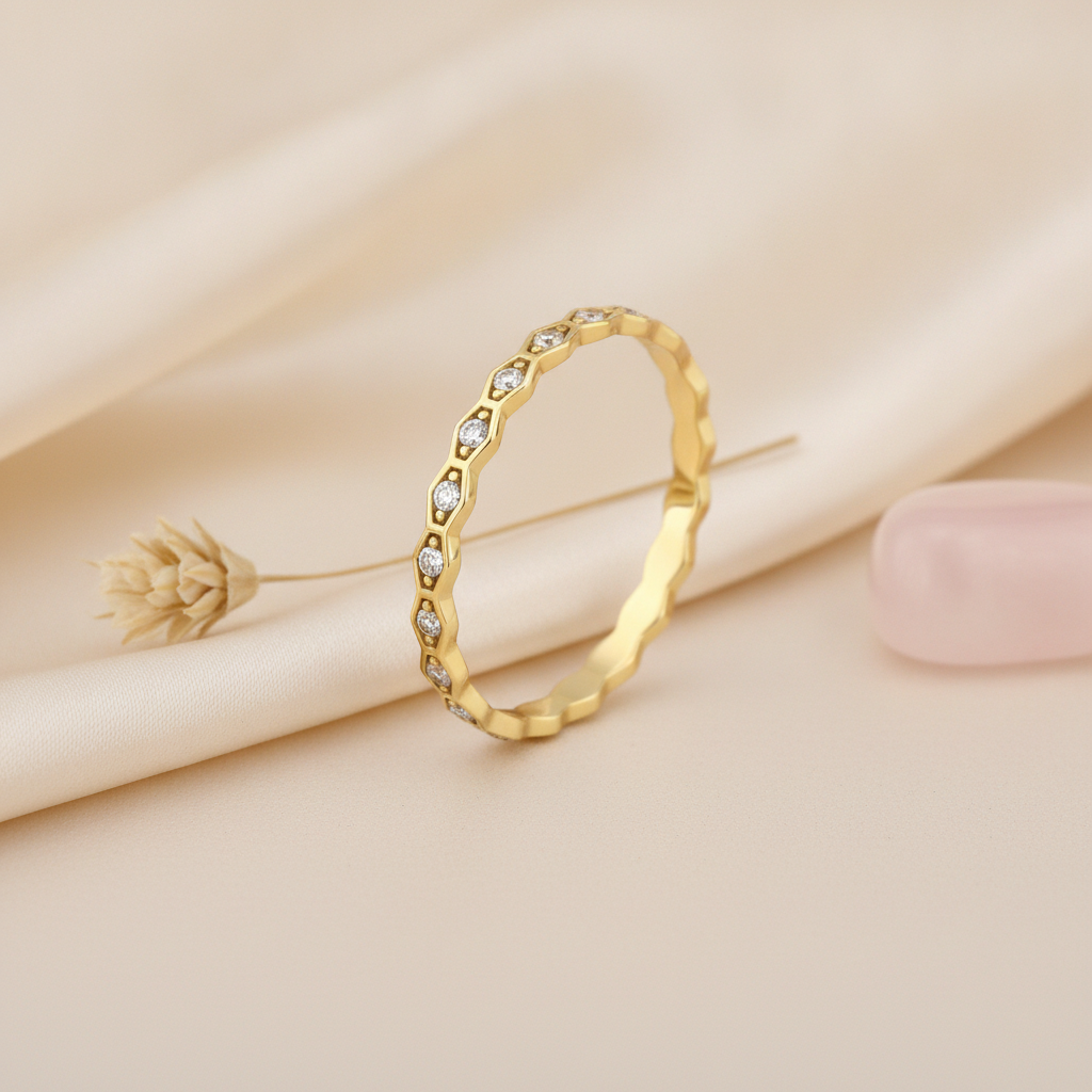 gold ring with a kite-shaped faceted crest and clear accent stones on blush silk with dried flowers and a pebble
