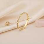 gold ring with a kite-shaped faceted crest and clear accent stones on blush silk with dried flowers and a pebble