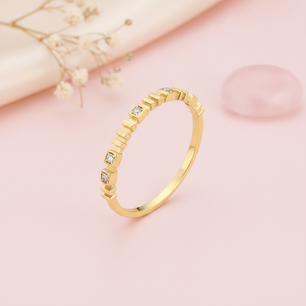 gold ring with raised vertical bar accents and small square-set clear stones on blush silk with dried flowers and rose quartz