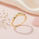 gold ring with scattered blue and clear stones on a smooth wave-shaped band on blush silk with dried flowers and rose quartz