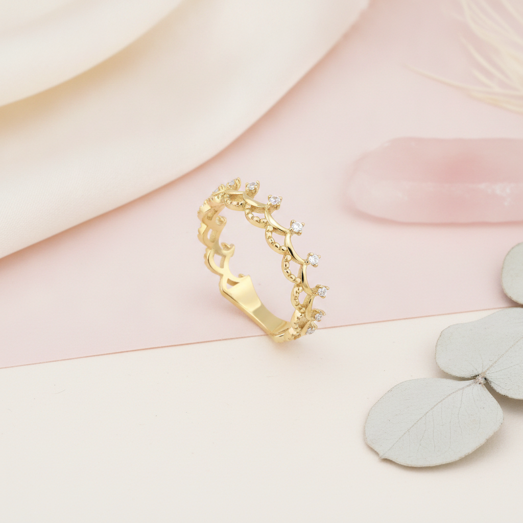 gold ring with beaded tiara-inspired arches and prong-set clear stones on a blush pink and cream background with rose quartz and dried leaves