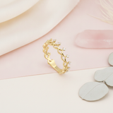 gold ring with beaded tiara-inspired arches and prong-set clear stones on a blush pink and cream background with rose quartz and dried leaves