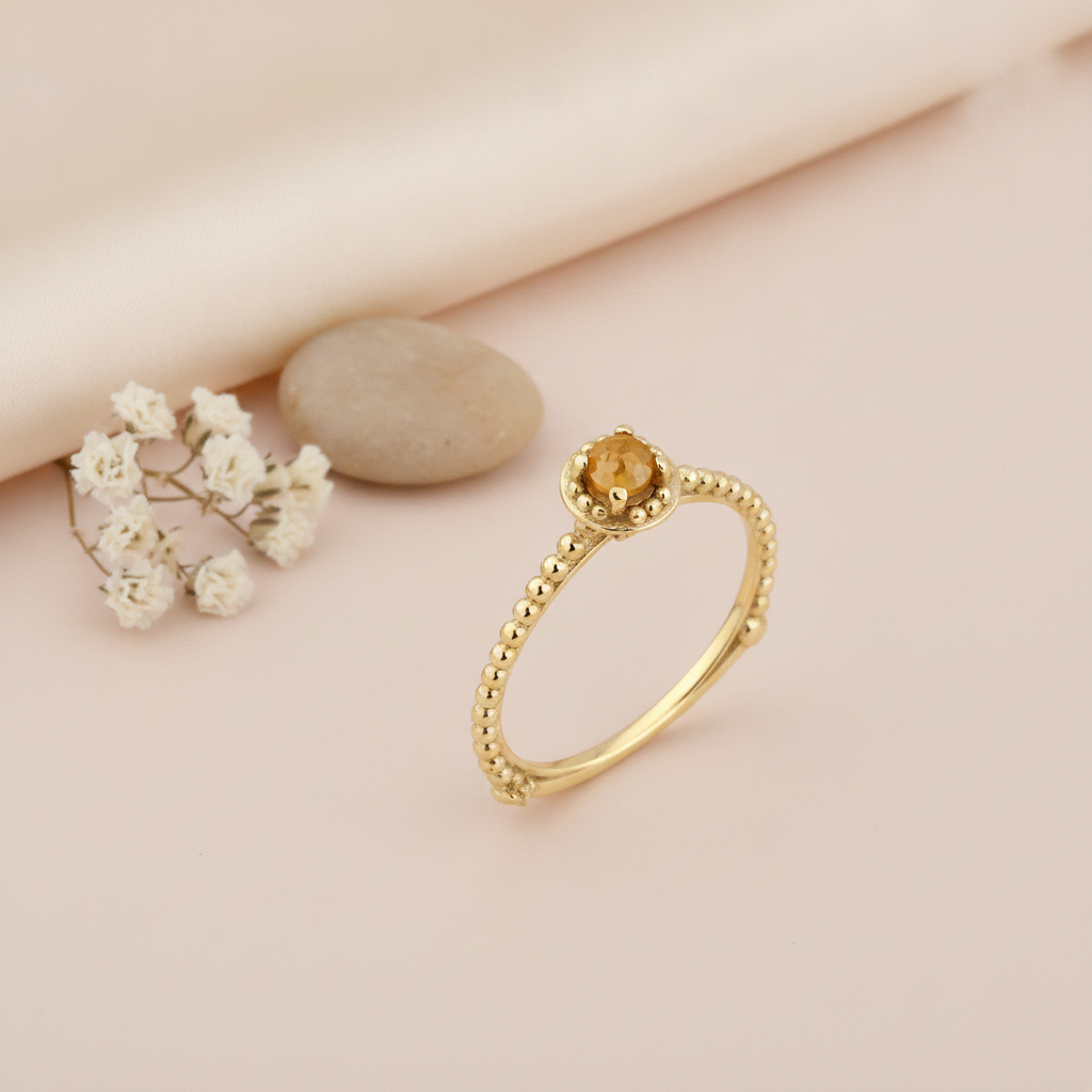 gold beaded ring with a round golden-yellow stone, styled with dried baby's breath and a stone on a blush background