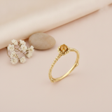 gold beaded ring with a round golden-yellow stone, styled with dried baby's breath and a stone on a blush background