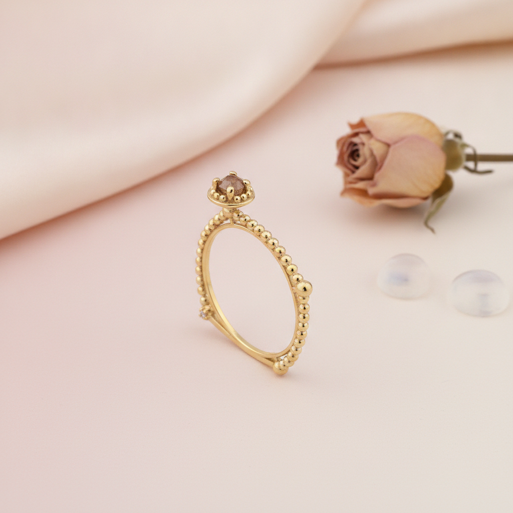 gold beaded ring with a crowned center stone, styled with a dried rose and clear stones on a blush background