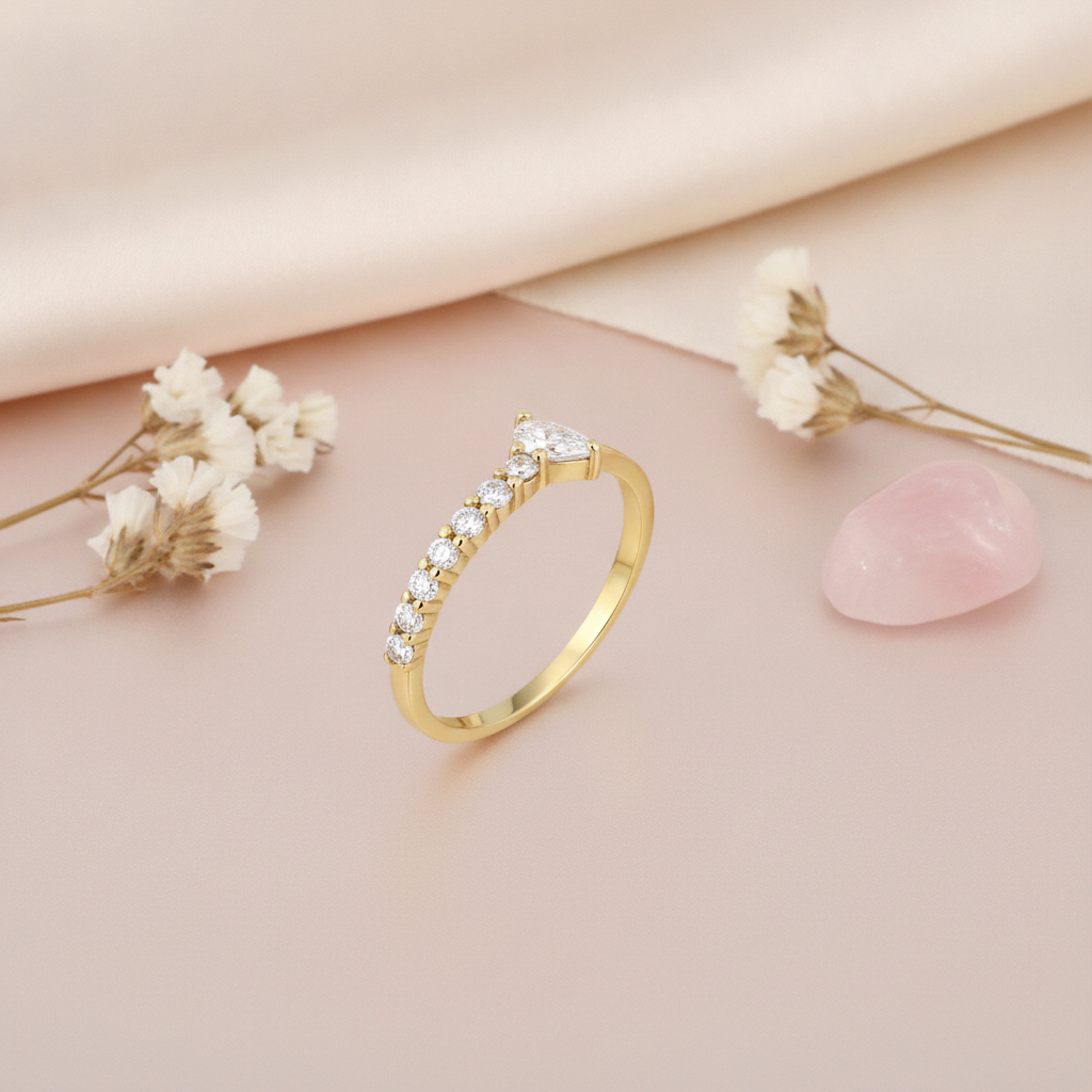 gold ring lined with pave stones rising to a pear-cut stone, styled with dried flowers and a pink stone on a blush background