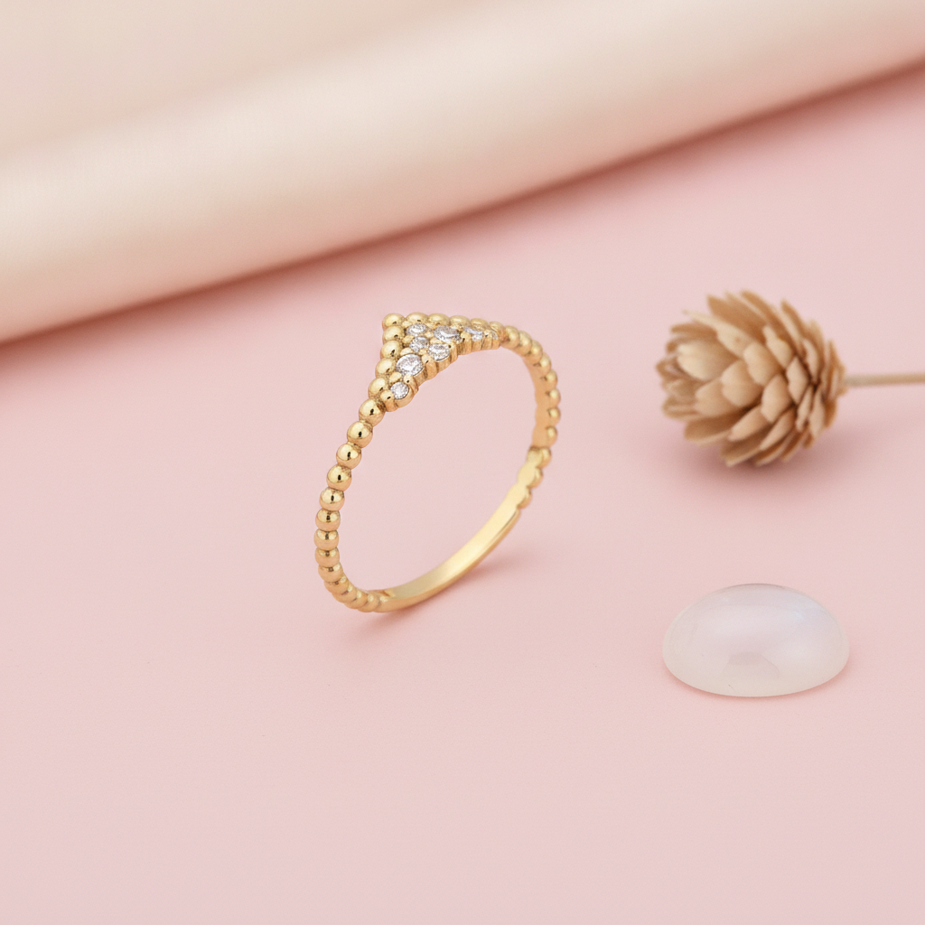 gold beaded ring with a chevron of pave stones, styled with a dried flower on a pink background
