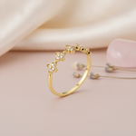gold ring with pave-set four-petal flower motifs, styled with dried lavender and a pink stone on a blush background