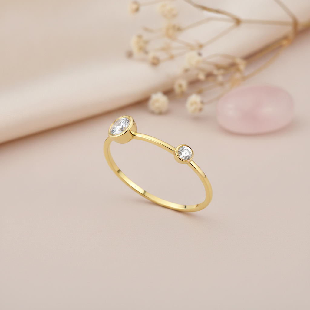 open gold ring with two bezel-set clear stones of contrasting size, styled with dried baby's breath and a pink stone on a blush background