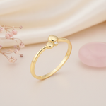 gold ring with two polished spheres and a clear stone accent, styled with dried baby's breath and a pink stone on a blush background