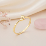 gold ring with two polished spheres and a clear stone accent, styled with dried baby's breath and a pink stone on a blush background