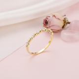 gold ring alternating polished beads and clear stones, styled with a dried rose on a blush background