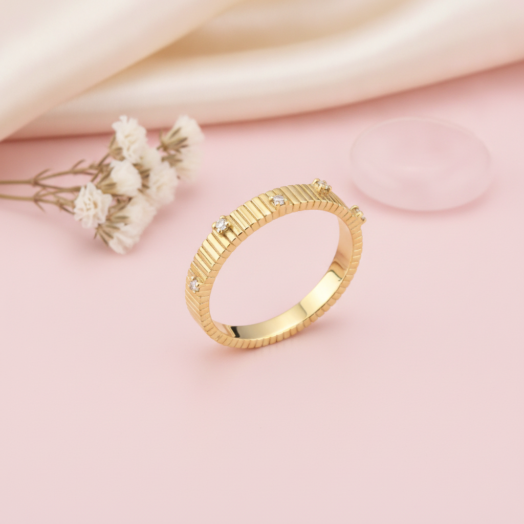 ribbed gold ring set with small clear stones at intervals, styled with dried baby's breath and a translucent stone on a pink background