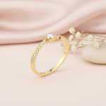 gold ring with a channel of clear stones and a crowned center stone, styled with dried baby's breath and a stone on a blush background