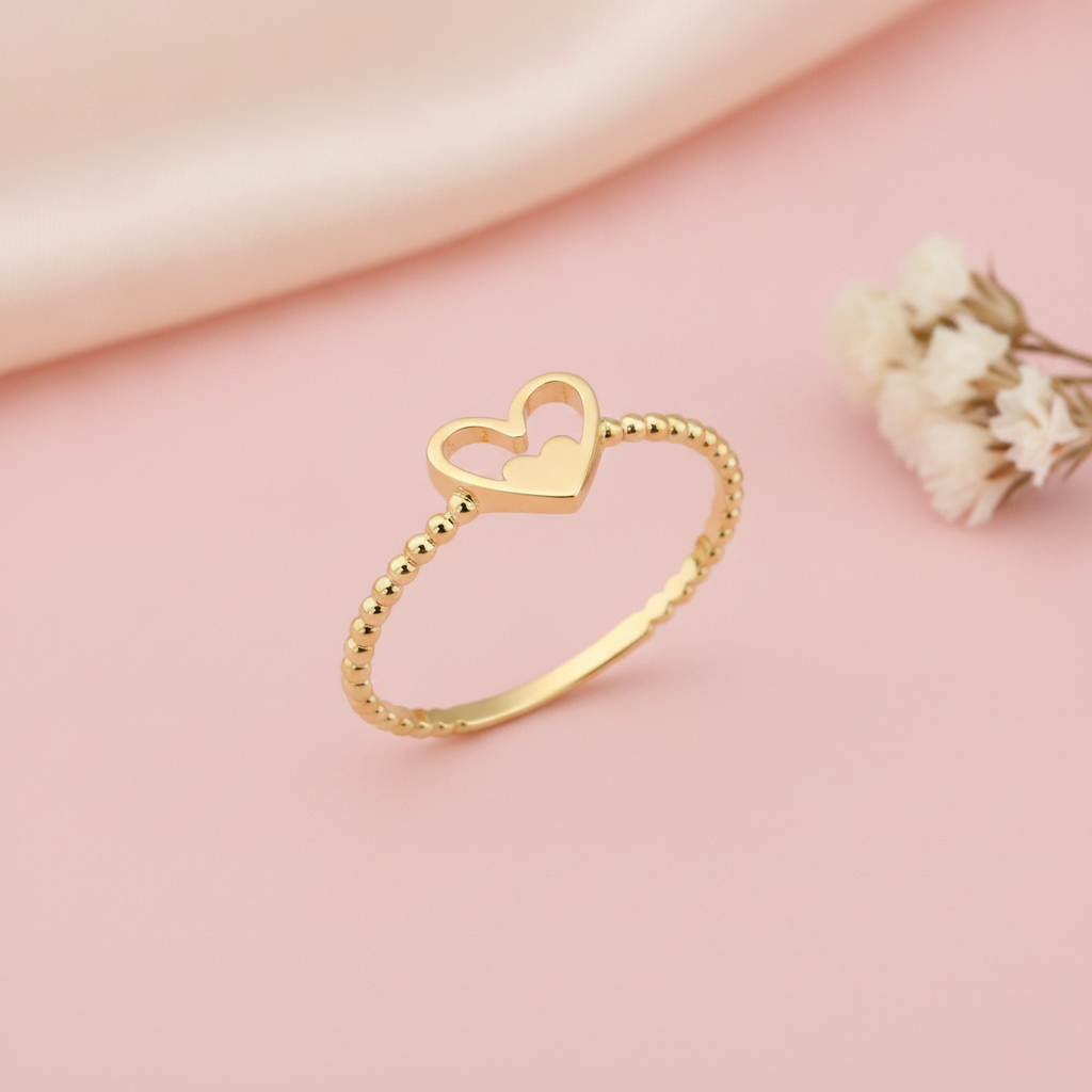 gold ring with an open heart cradling a smaller solid heart, styled with dried baby's breath on a pink background