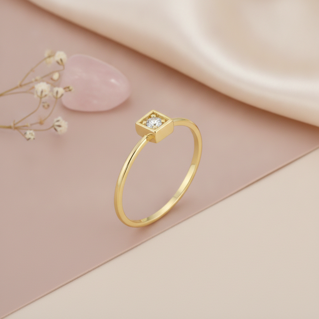 gold ring with a clear stone set in a square frame, styled with dried baby's breath, a stone, and dried grass on a blush background