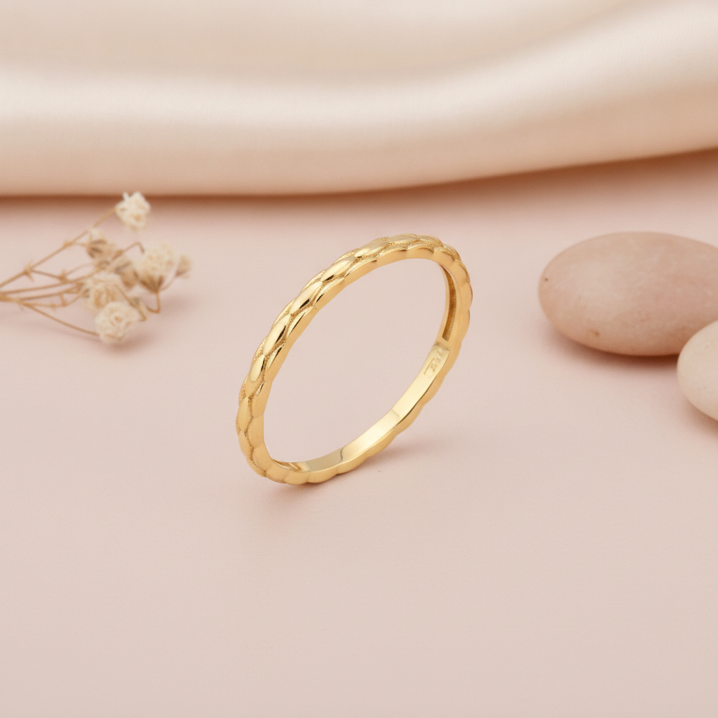 gold ring with a braided texture tapering to a smooth band, styled with a dried rose and stones on a blush background