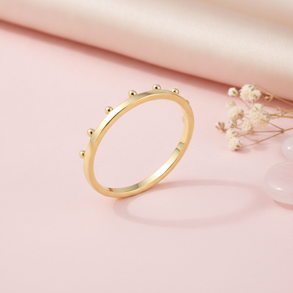 gold ring with raised golden spheres along the edge, styled with dried baby's breath and a pink stone on a blush background