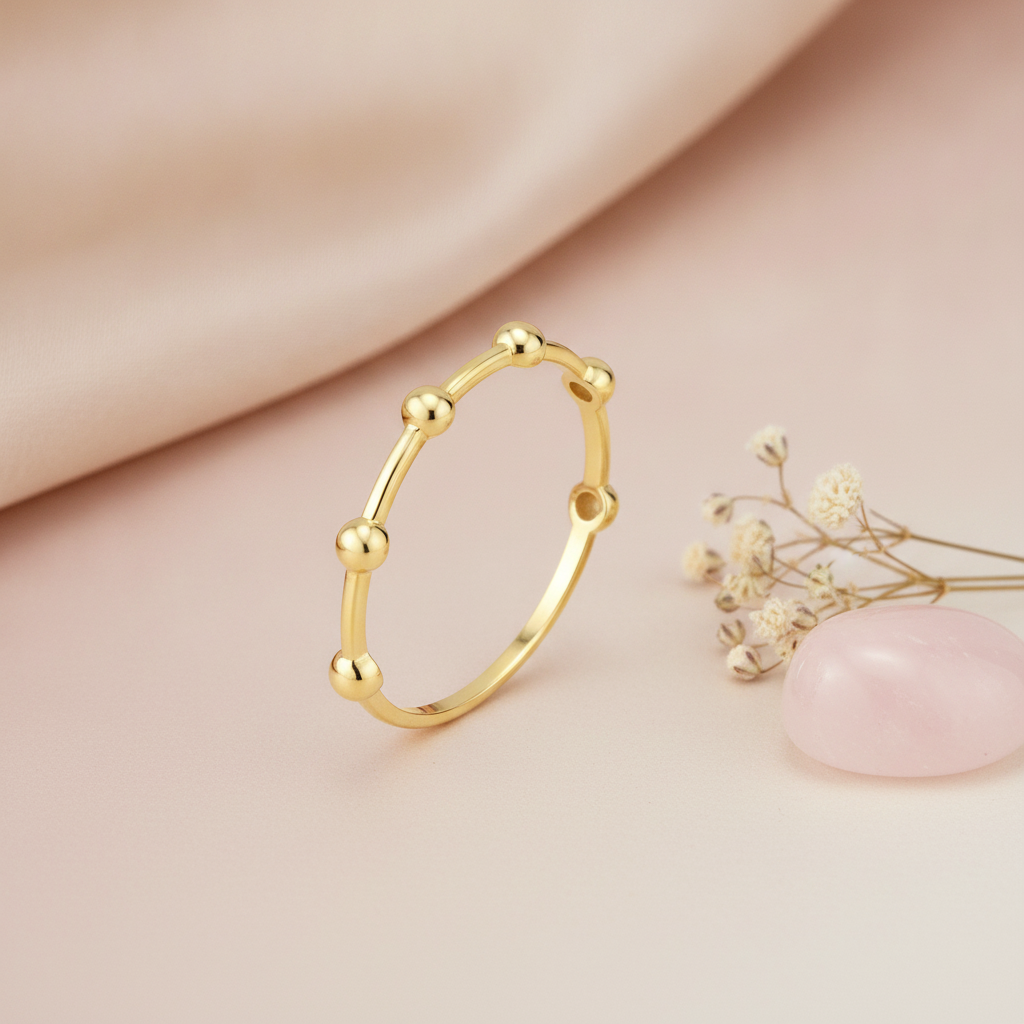 gold ring punctuated with polished golden spheres, styled with dried baby's breath and a pink stone on a blush background
