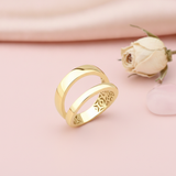 gold double-band ring with an open silhouette, styled with a dried rose and a pink stone on a pink background