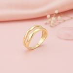 gold ring with two undulating wave bands, styled with a peony and a pink stone on a blush background