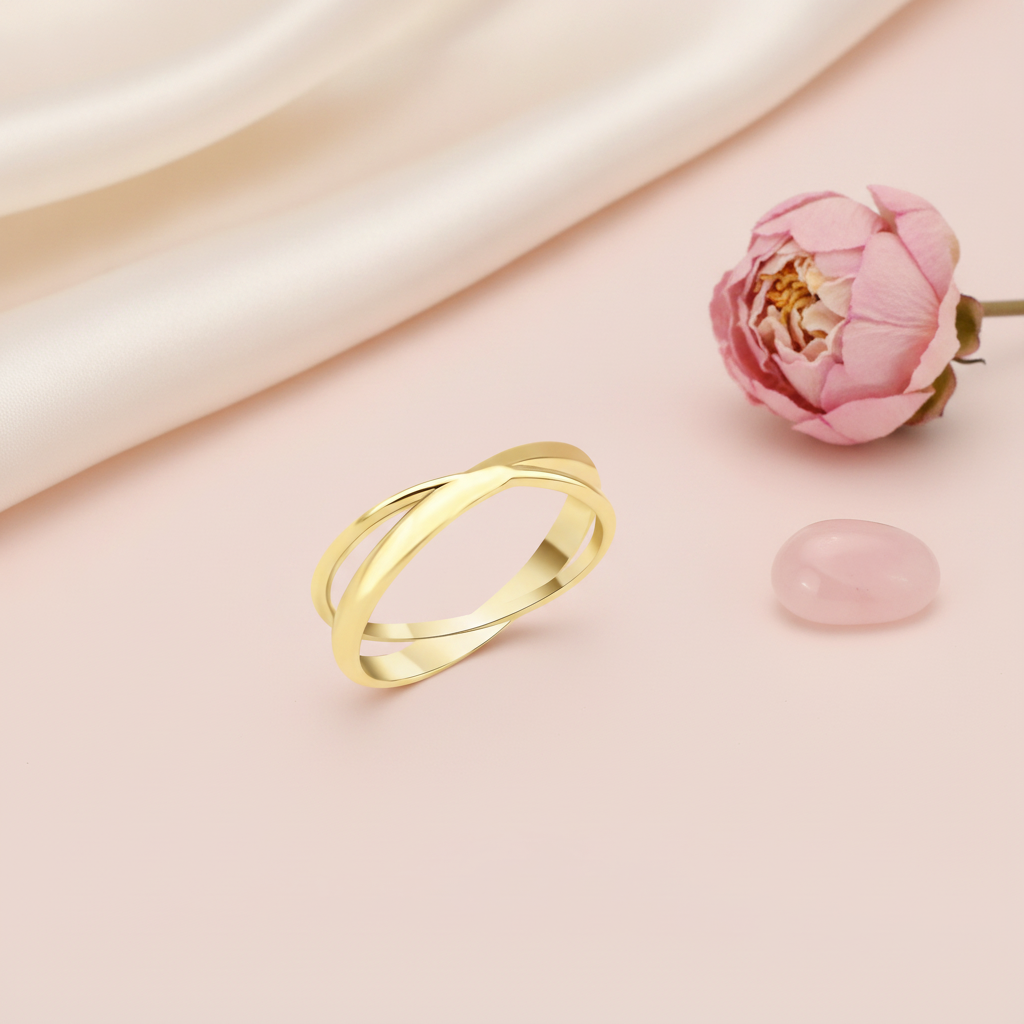 gold crossover ring with two fluid bands, styled with dried baby's breath and a pink stone on a blush background