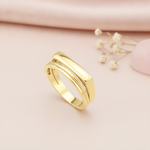 gold ring with a flat bar floating over a curved band, styled with a eucalyptus leaf and a pink stone on a cream background