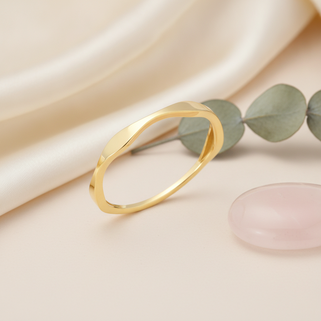 gold ring with an undulating wave design, styled with dried baby's breath and a pink stone on a blush background