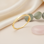gold ring with an undulating wave design, styled with dried baby's breath and a pink stone on a blush background