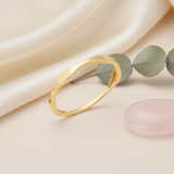 gold ring with an undulating wave design, styled with dried baby's breath and a pink stone on a blush background