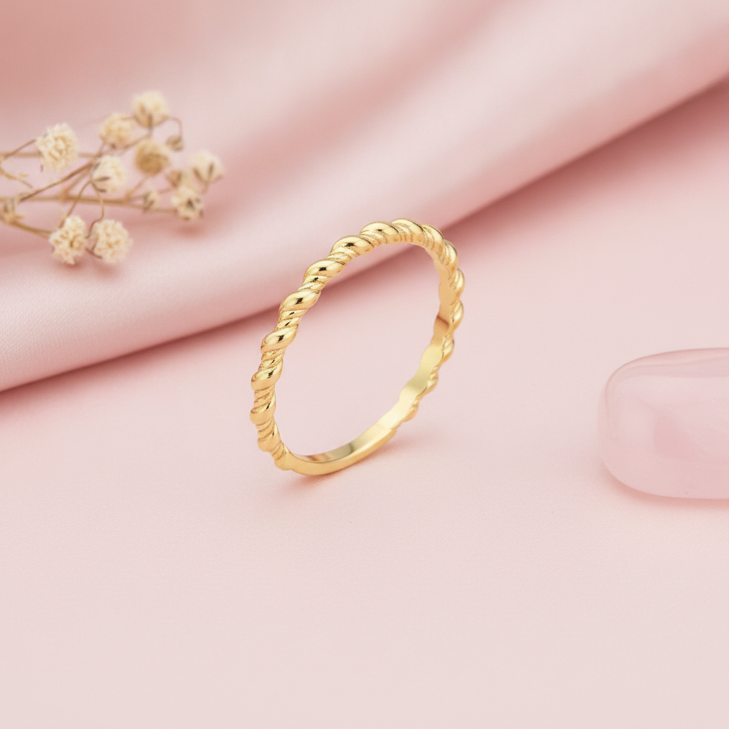 gold twisted-rope ring tapering to a smooth polished band, styled with a dried rose and stones on a cream background