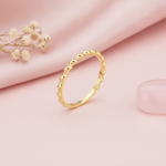gold twisted-rope ring tapering to a smooth polished band, styled with a dried rose and stones on a cream background