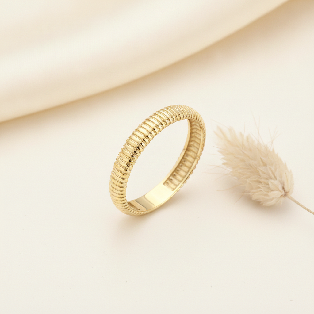 gold ring with fine ribbed texture, styled with a dried grass sprig on a cream background