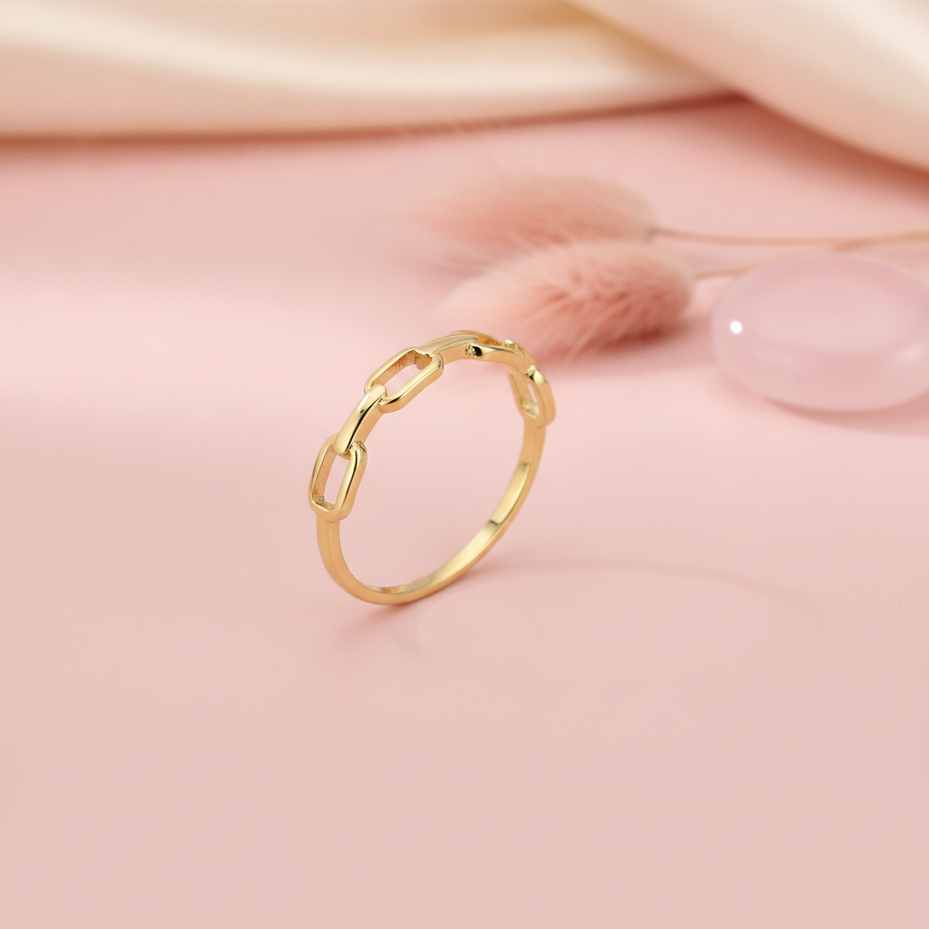 gold ring with open paperclip chain links, styled with dried grass and a pink stone on a blush background