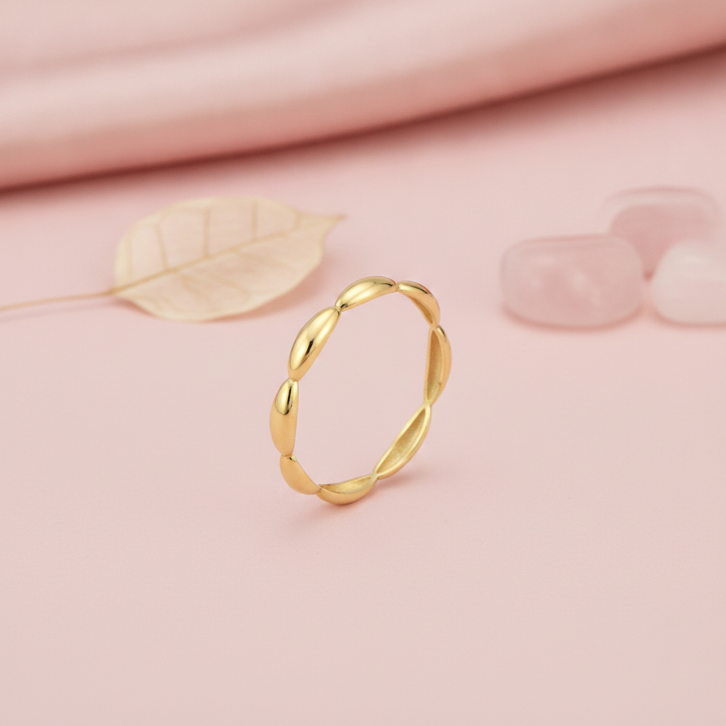 gold ring with smooth elongated pod links, styled with a dried leaf and translucent stones on a pink background