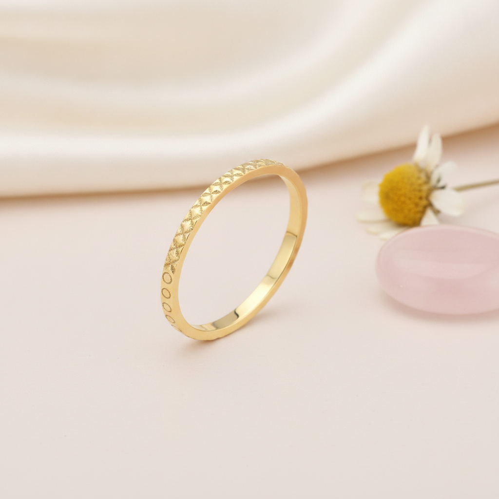 gold ring with carved circle and geometric cross texture, styled with a daisy and a pink stone on a blush background
