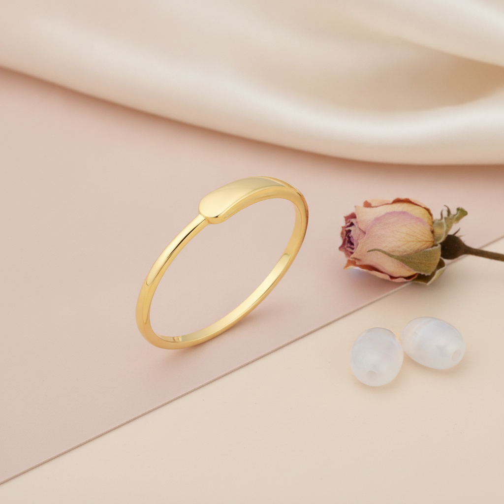 gold ring with a smooth teardrop motif, styled with a dried rose and pearl-like stones on a blush background