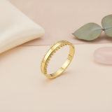 gold ring with a smooth center flanked by beaded borders, styled with a eucalyptus leaf and a pink stone on a blush background