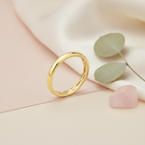 gold band ring with a subtle carved interior, styled with eucalyptus leaves and a rose quartz stone on a cream background