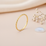 slender etched gold Raya ring on a blush background with draped satin fabric and a moonstone cabochon