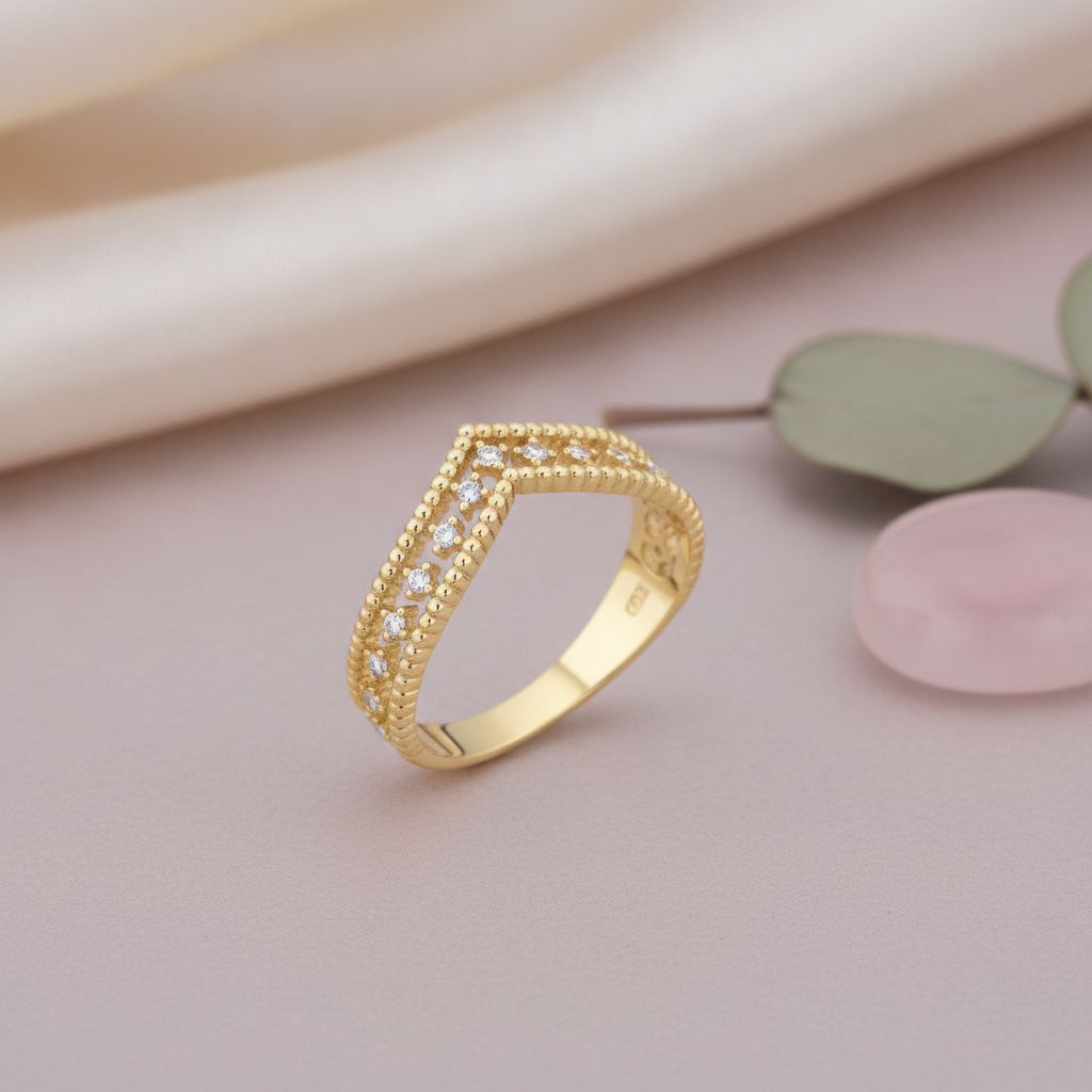 gold chevron ring with beaded borders and White CZ stones on a mauve background with draped satin fabric, a eucalyptus leaf, and a pink stone