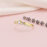 gold V-shaped chevron ring with graduating round stones on a blush background with draped satin fabric and lavender sprigs